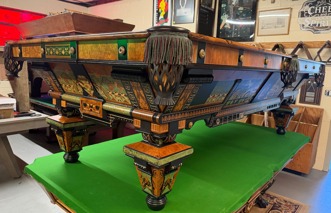 Intricately detailed Art Deco style restored pool table featuring decorative green inlay paneling and tassel-fringed leather pockets.
